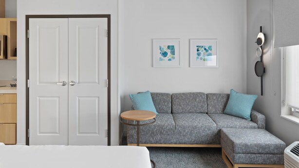 Une chambre moderne avec un canapé gris, une petite table ronde et une armoire blanche.