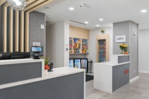 A reception area with a counter, a computer, a small plant, and a wall with a patterned design. - Towneplace Suites By Marriott White Hall (White Hall)