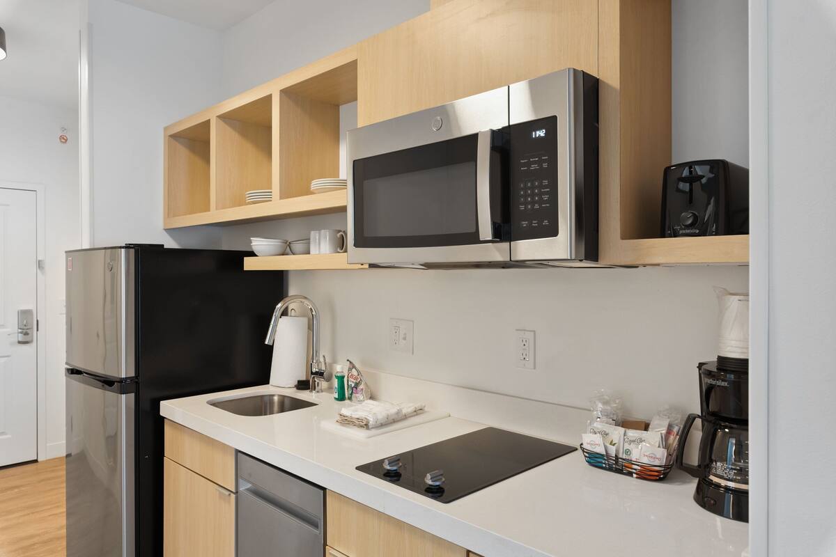 A modern kitchen with a stainless steel refrigerator, a black microwave, and a coffee maker.