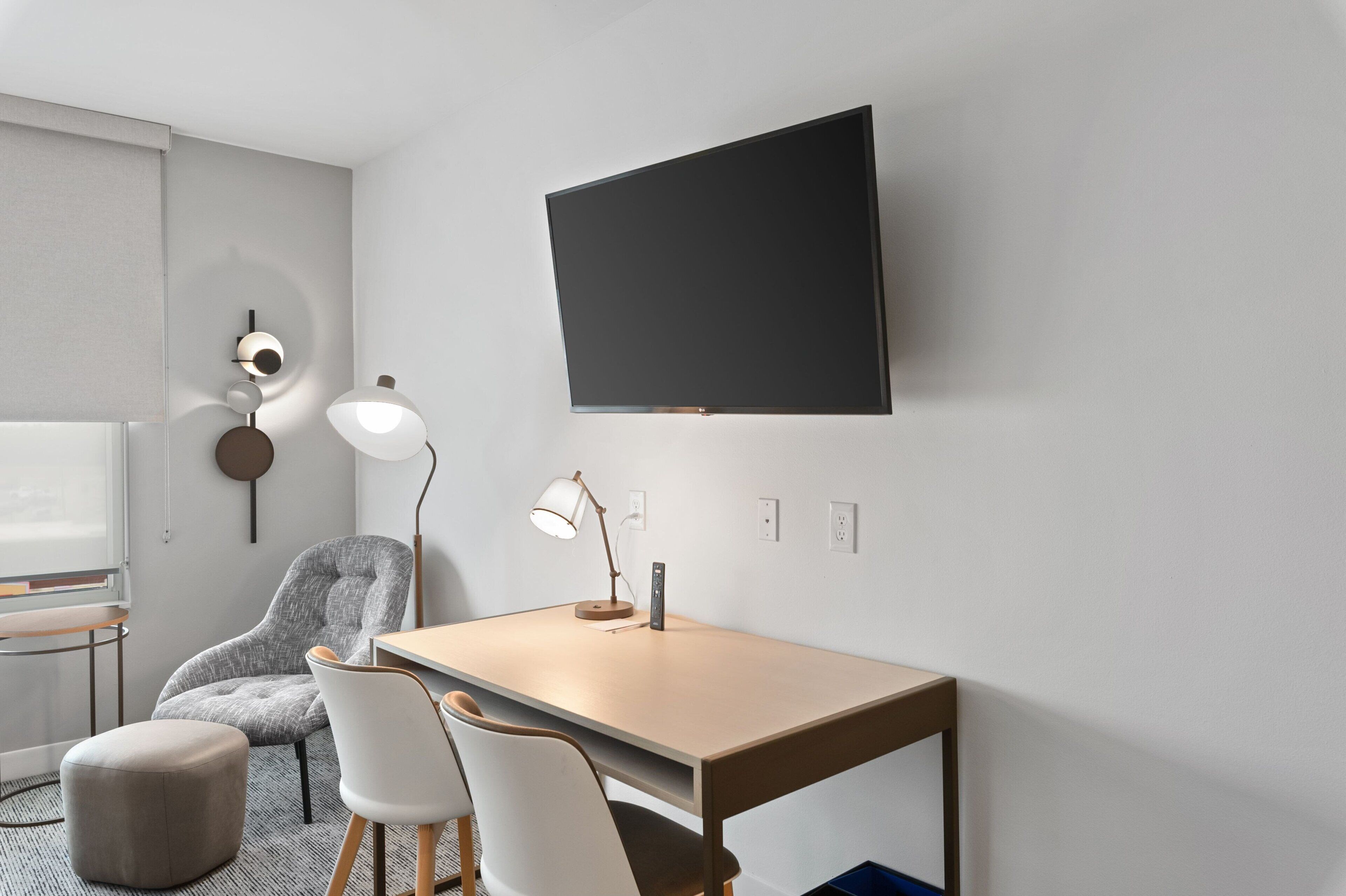 Ein modernes Zimmer mit Schreibtisch, zwei Stühlen, einer Lampe, einem Fernseher und einer runden Wanddekoration.