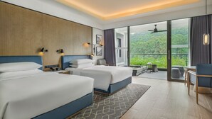 Une chambre d’hôtel moderne avec deux lits, un balcon donnant sur un espace verdoyant et un coin salon avec une table et des chaises.
