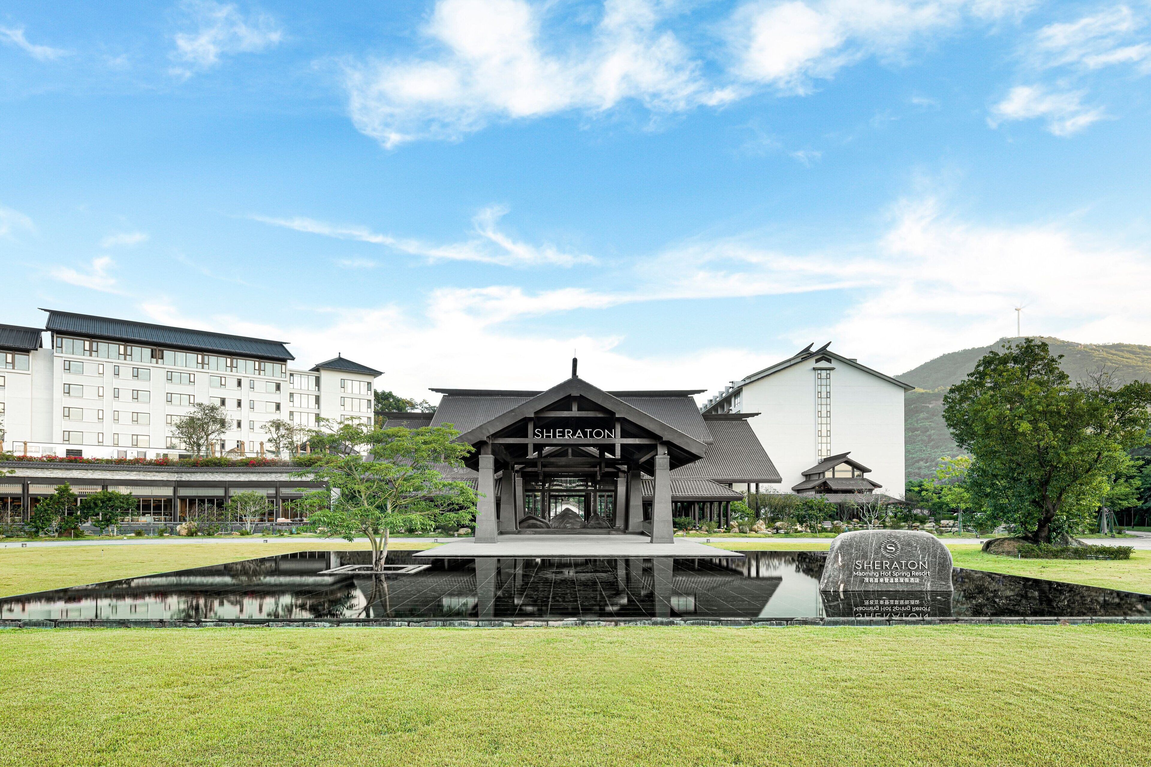 Un hotel con una entrada de estilo japonés tradicional, un estanque en primer plano y edificios modernos al fondo.
