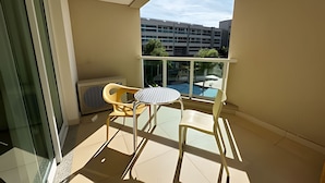 A balcony with a table and chairs, a view of a parking garage, and a pool in the background. - Brisas do Lago - apartamento 2 (Brasília)
