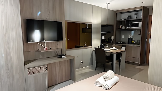 A modern hotel room with a flat-screen TV, a dining area, and a kitchen area. - Brisas do Lago - apartamento 2 (Brasília)