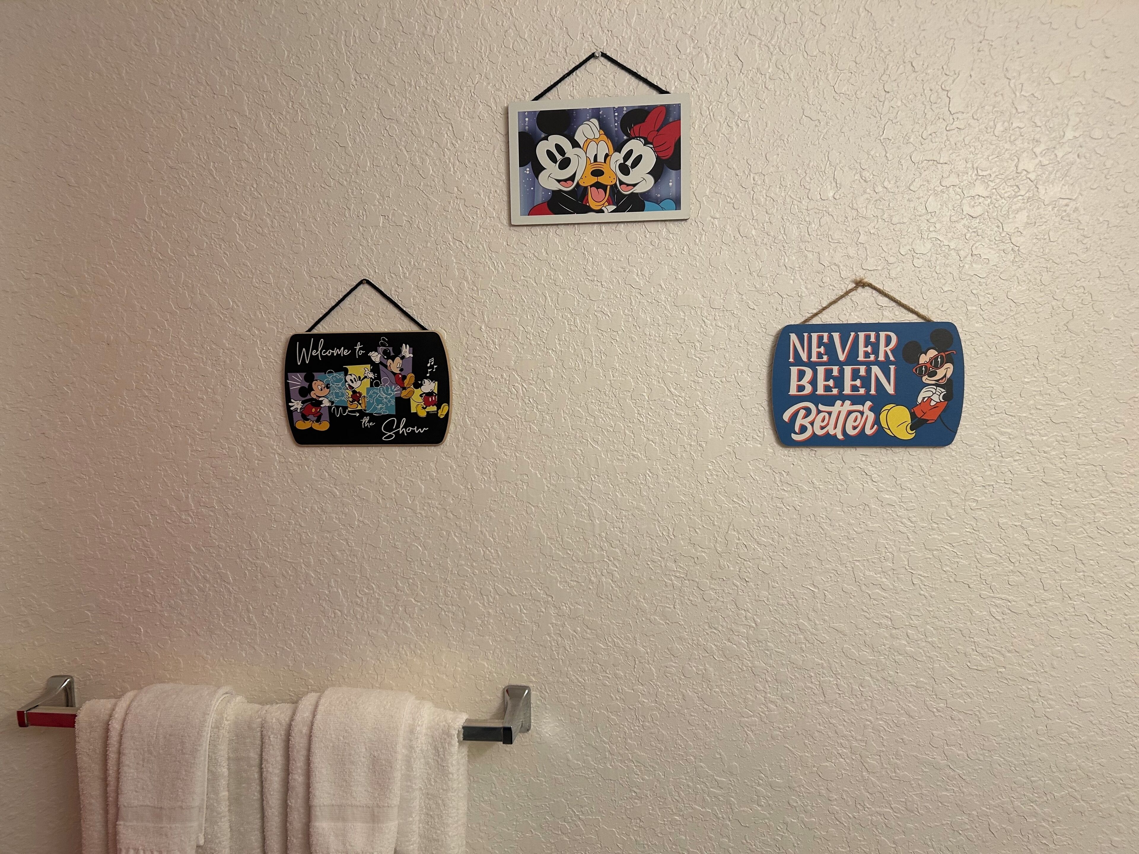 Three wall decorations featuring Disney characters, a towel rack, and a towel.