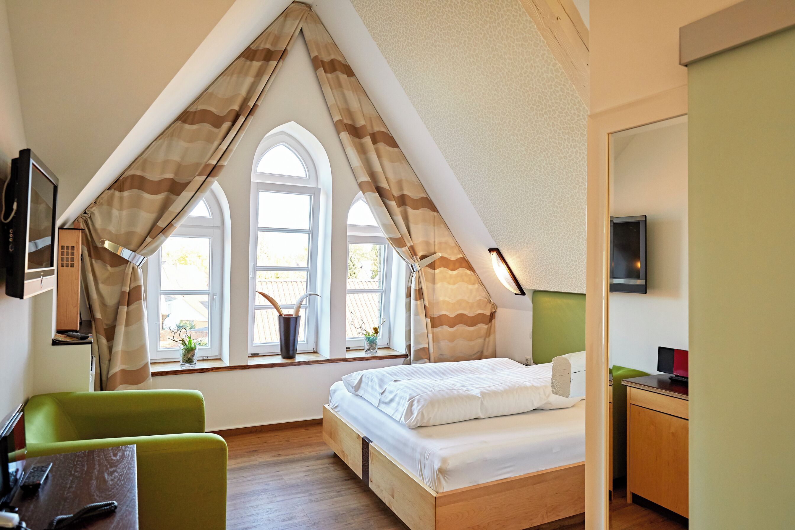 A bedroom with a sloped ceiling, a bed, a desk, and a chair.