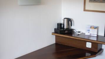 A small office space with a wooden desk, a black chair, a coffee maker, and a framed picture on the wall.