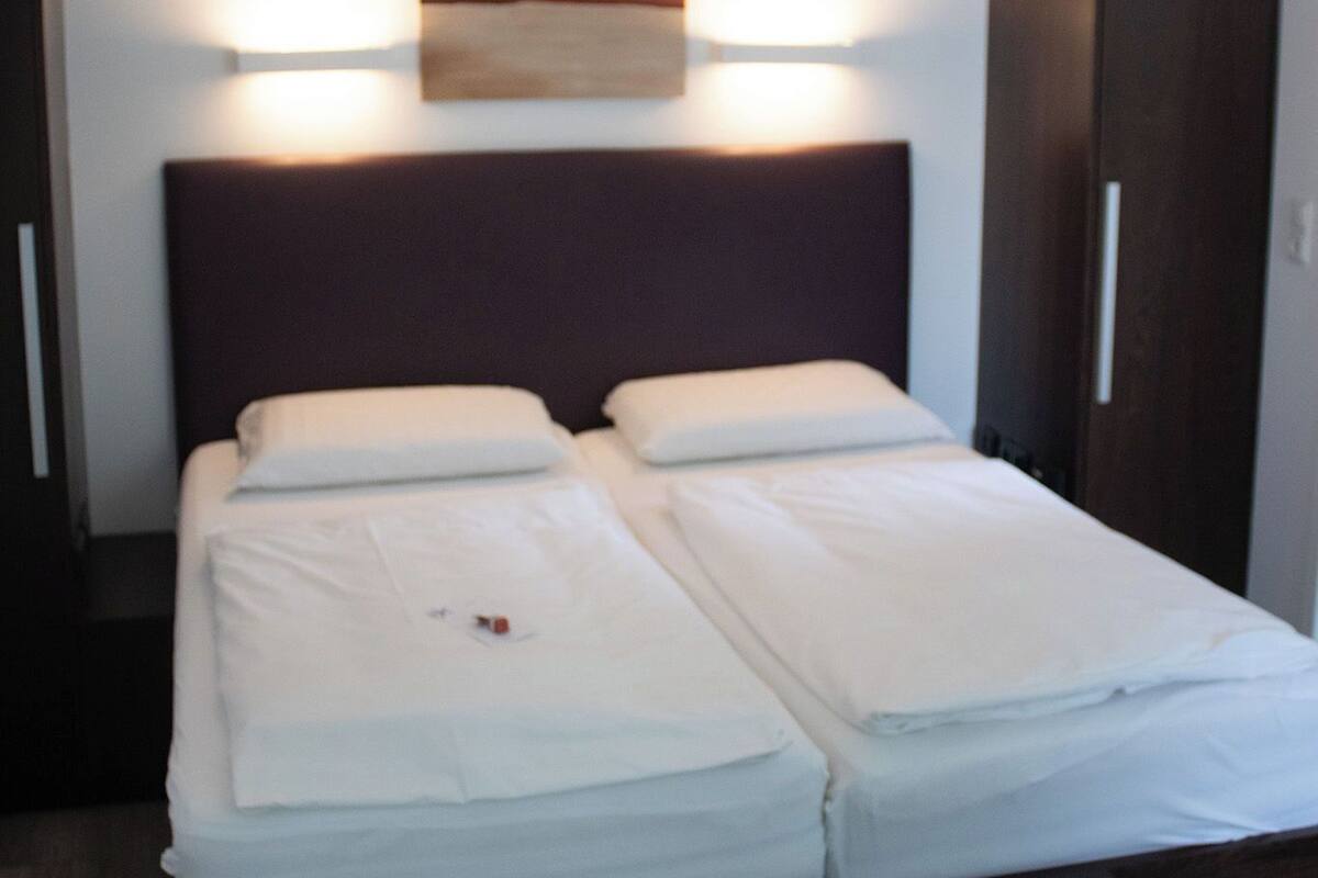 En dubbelsäng med vita sängkläder, en mörk sänggavel och två sänglampor.