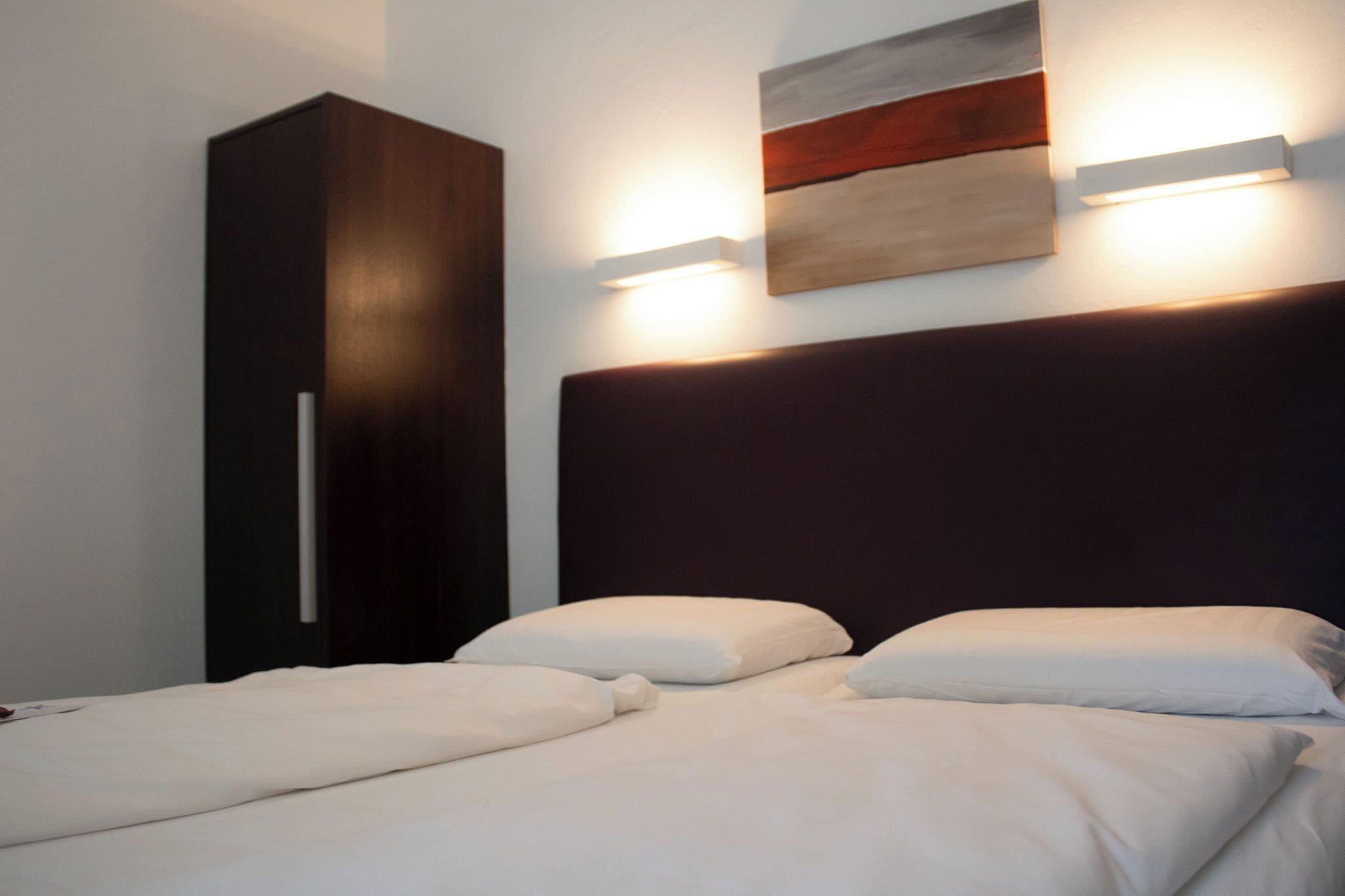 Ein Hotelzimmer mit Bett, Kleiderschrank und Wandleuchte.