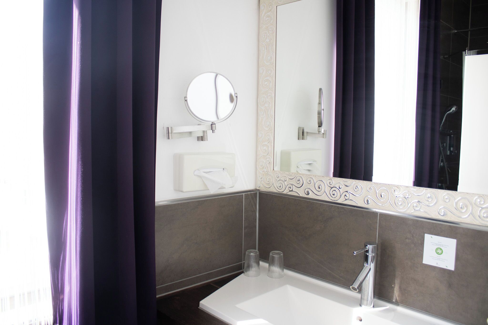 A bathroom with a white sink, a round mirror, and two clear glasses on the counter.