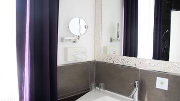 A bathroom with a white sink, a round mirror, and two clear glasses on the counter.
