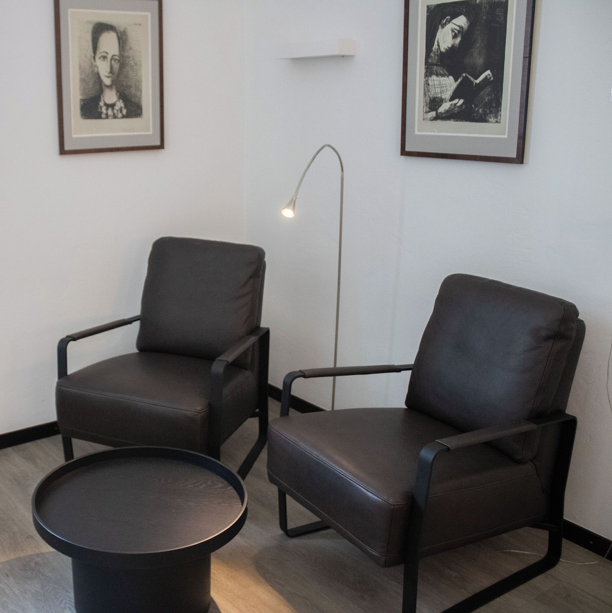 Dos sillones de cuero negro y una pequeña mesa redonda en una habitación con paredes blancas.