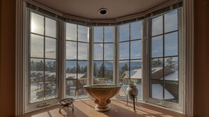 A bay window with a large vase and a small table, overlooking a snowy village. - Marble Canyon 3 Bdrm|Sleeps 8 (12 inc kids): Unit 102P1 (Fairmont Hot Springs)