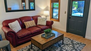 A living room with a red leather couch, a wooden coffee table with a plant, a patterned rug, a lamp, and a door with a window view. - Bluebird Day - River Otter, Charming 1BR duplex in Old Downtown Bend (Bend)