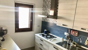 Una cocina moderna con estufa a gas, pileta de acero inoxidable y alacenas de madera clara.