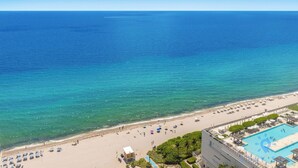 Un hôtel situé en bord de mer, doté d’une piscine, de parasols et offrant une vue dégagée sur l’océan.