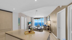 Une cuisine moderne dotée d’un îlot central, d’un coin repas et de grandes fenêtres offrant une vue sur la mer.