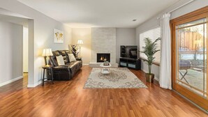 A living room with a fireplace, leather sofa, TV, and a large window. - @ Marbella Lane - 4BR SiliconValley Gem|Pool House (San Jose)