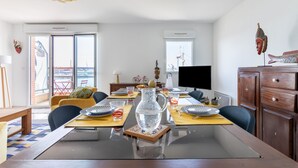 A modern dining area with a glass-top table, wooden chairs, and a pitcher of water. - L'Airelle - Two Bedroom Apartment, Sleeps 4 (Saint-Malo)