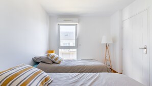 A bedroom with two beds, a window, a lamp, and a wardrobe. - L'Airelle - Two Bedroom Apartment, Sleeps 4 (Saint-Malo)
