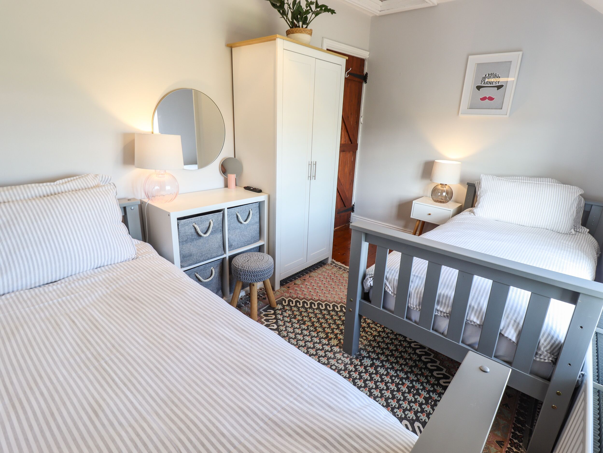 A bedroom with two beds, a wardrobe, a mirror, and a small stool.