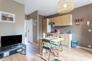Una cucina moderna con mobili in legno, un'area pranzo con tavolo e sedie, un televisore su un mobile basso e una lampada a sospensione in vimini.