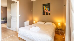 A bedroom with a bed, two bedside lamps, a painting of parrots, and a door leading to another room. - Rochebonne - One Bedroom Apartment, Sleeps 4 (Saint-Coulomb)