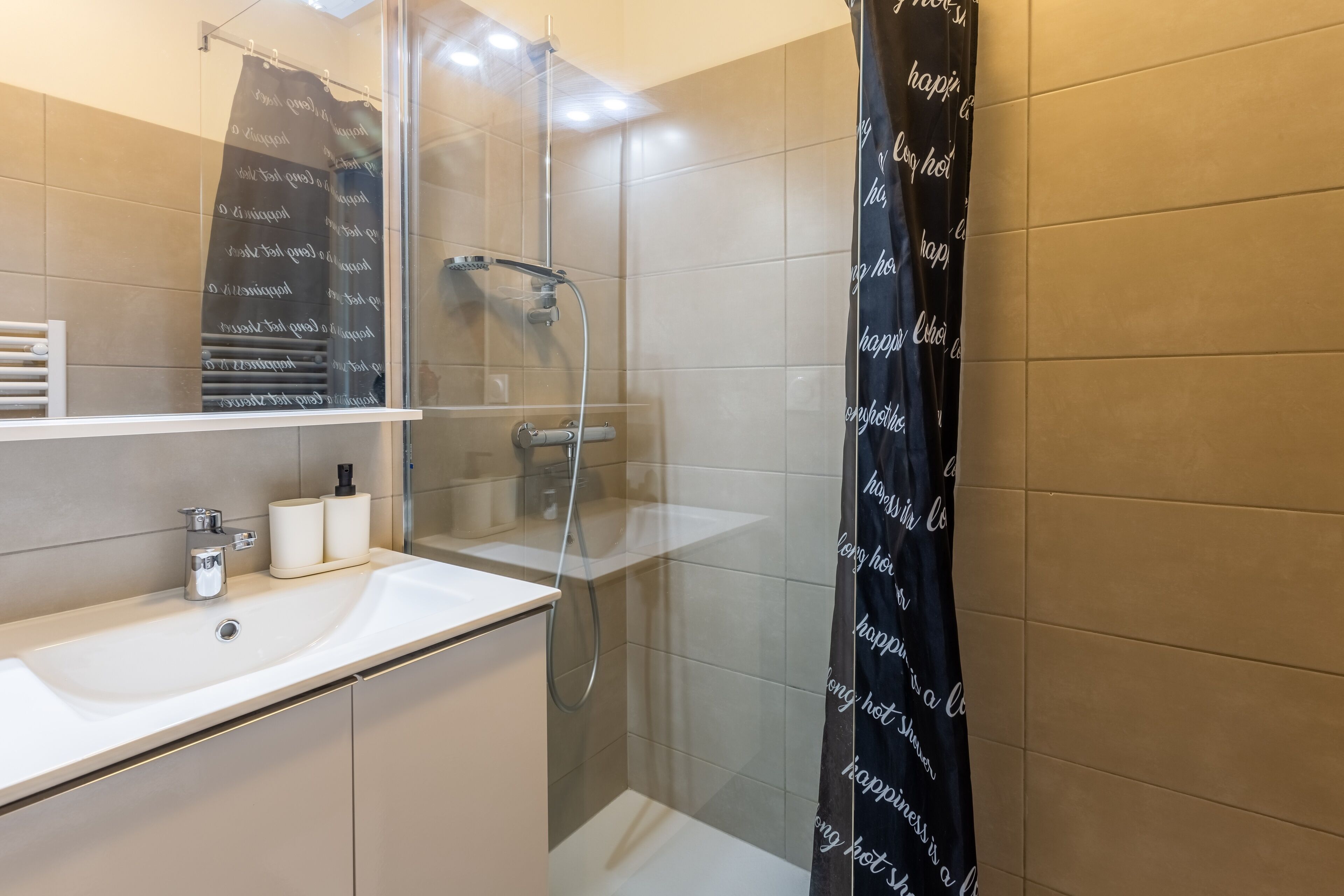 Een moderne badkamer met een douchecabine van glas, een witte wastafel en een spiegel erboven.