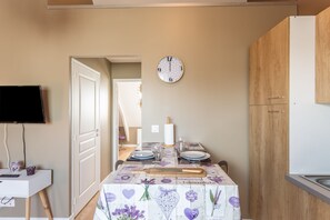 Una cocina con una mesa de comedor lista para dos personas, un reloj en la pared y un televisor montado.