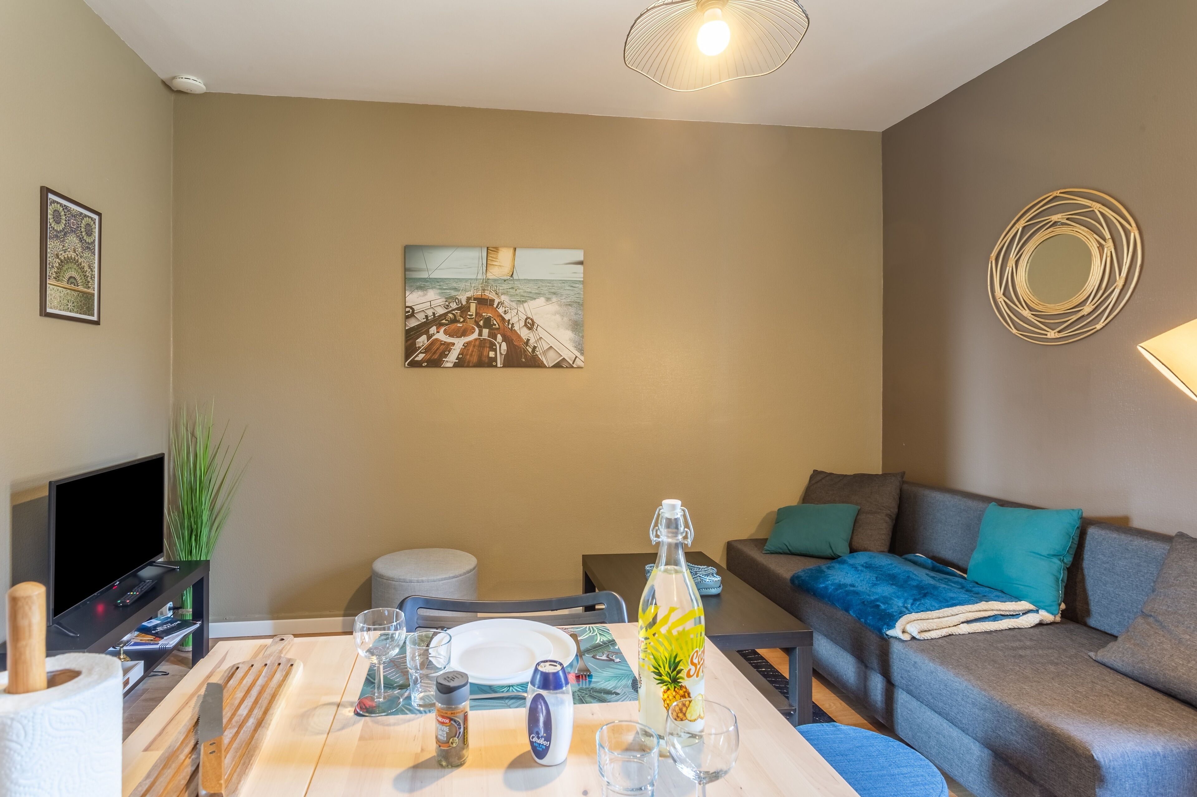 Een eetgedeelte met een tafel gedekt voor twee personen, een schilderij aan de muur en een bank met een plaid.