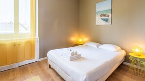 A bedroom with a bed, a painting of a boat on the beach, and a window with a yellow curtain. - Minihic - appartement avec jardin (Saint-Coulomb)