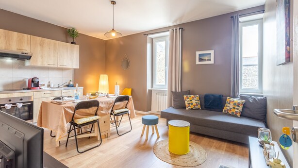 A modern apartment with a kitchen, dining area, and living room. It features a sofa, a dining table with chairs, a TV, and a window with curtains. - Minihic - appartement avec jardin (Saint-Coulomb)