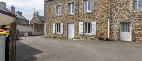 A stone building with multiple windows and doors, a paved driveway, and a small garden area.