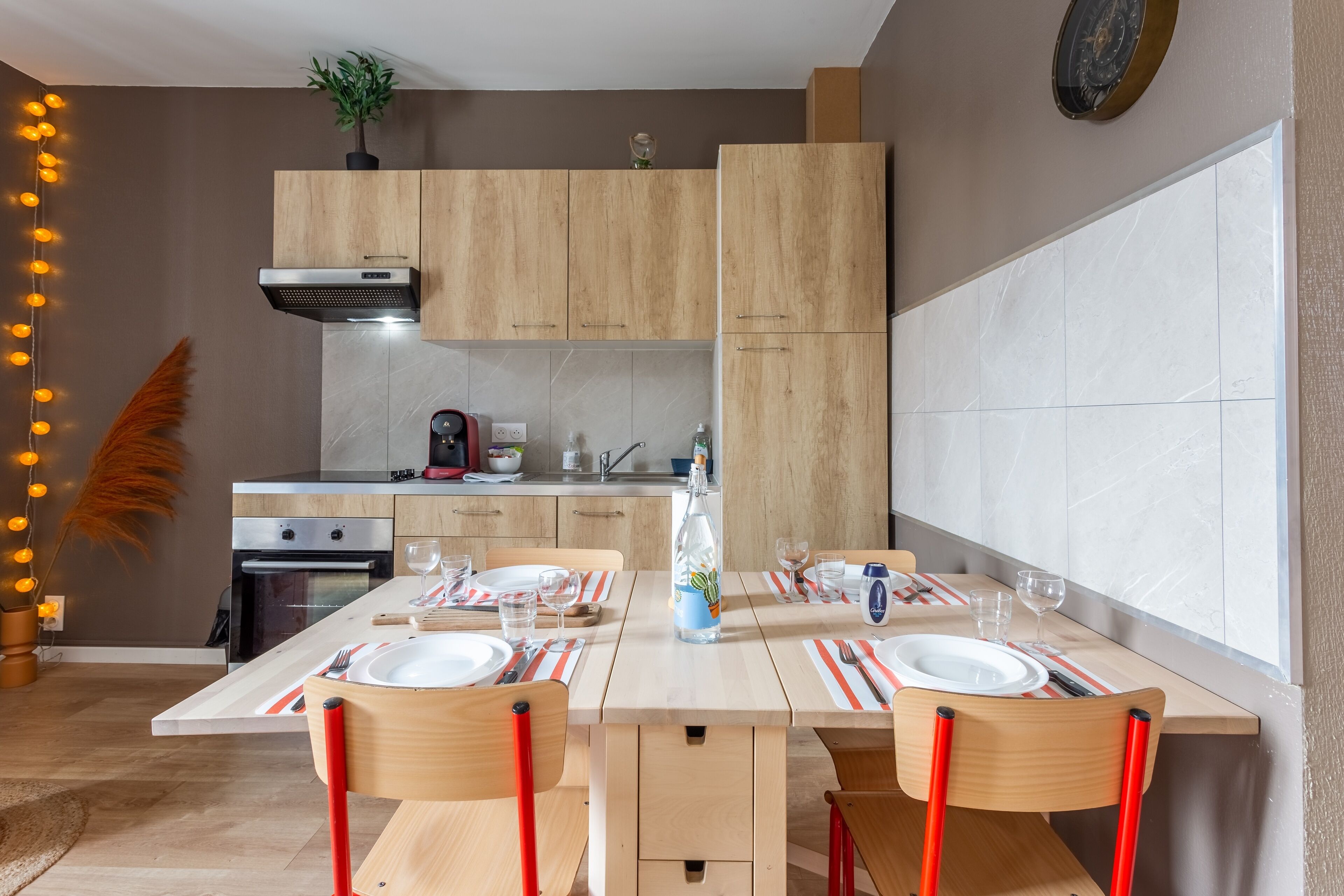 A modern kitchen with wooden cabinets, a built-in oven, and a dining area with striped placemats and red chairs.