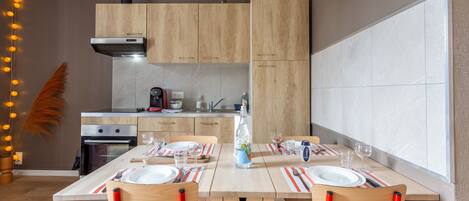 A modern kitchen with wooden cabinets, a built-in oven, and a dining area with striped placemats and red chairs.