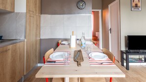A modern kitchen with wooden cabinets, a tiled backsplash, and a dining area with a long table set for four.