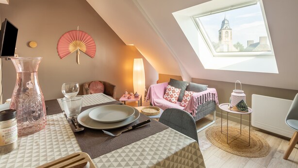 A cozy loft bedroom with a dining area, a large window with a city view, and a decorative fan. - Varde - appartement avec jardin (Saint-Coulomb)