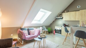 A cozy loft apartment with a sloped ceiling, a dining area with a table and chairs, a kitchen with wooden cabinets, and a large skylight. - Varde - appartement avec jardin (Saint-Coulomb)