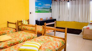 A room with four wooden beds with floral bedding, a small table with two chairs, a painting of a landscape, and a window with curtains. - Ribeiro Lugar de Paz Casa 1 (Arraial do Cabo)