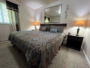 A bedroom with a large bed, two bedside tables with lamps, a mirror on the wall, and a window with curtains. - Wooded Hideaway & Gateway to Adventure. (Skandia)