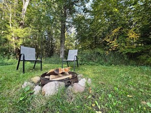 Un espace extérieur aménagé avec deux chaises et un foyer entouré de rochers et d’herbe.