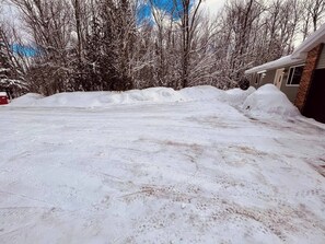 Un camino de entrada residencial cubierto de nieve, con un garaje y árboles al fondo.