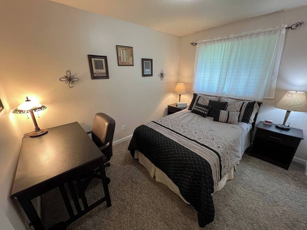 A bedroom with a bed, a desk, two nightstands, and a chair.