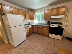 A kitchen with wooden cabinets, a white refrigerator, a microwave, a stove, and a sink. - Wooded Hideaway & Gateway to Adventure. (Skandia)