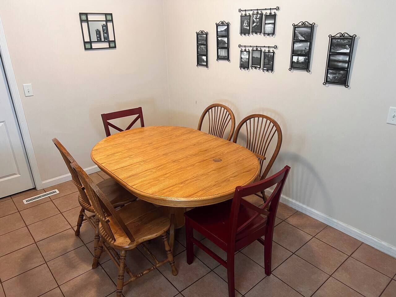 Een eetruimte met een ronde houten tafel en vier stoelen, een aan de muur bevestigd fotolijstje, en een deur met ventilatie.