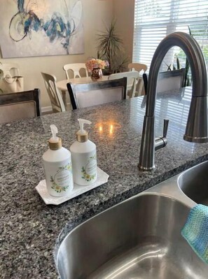 Une cuisine dotée de plans de travail en granit, d’un évier en acier inoxydable et de deux distributeurs de savon liquide.
