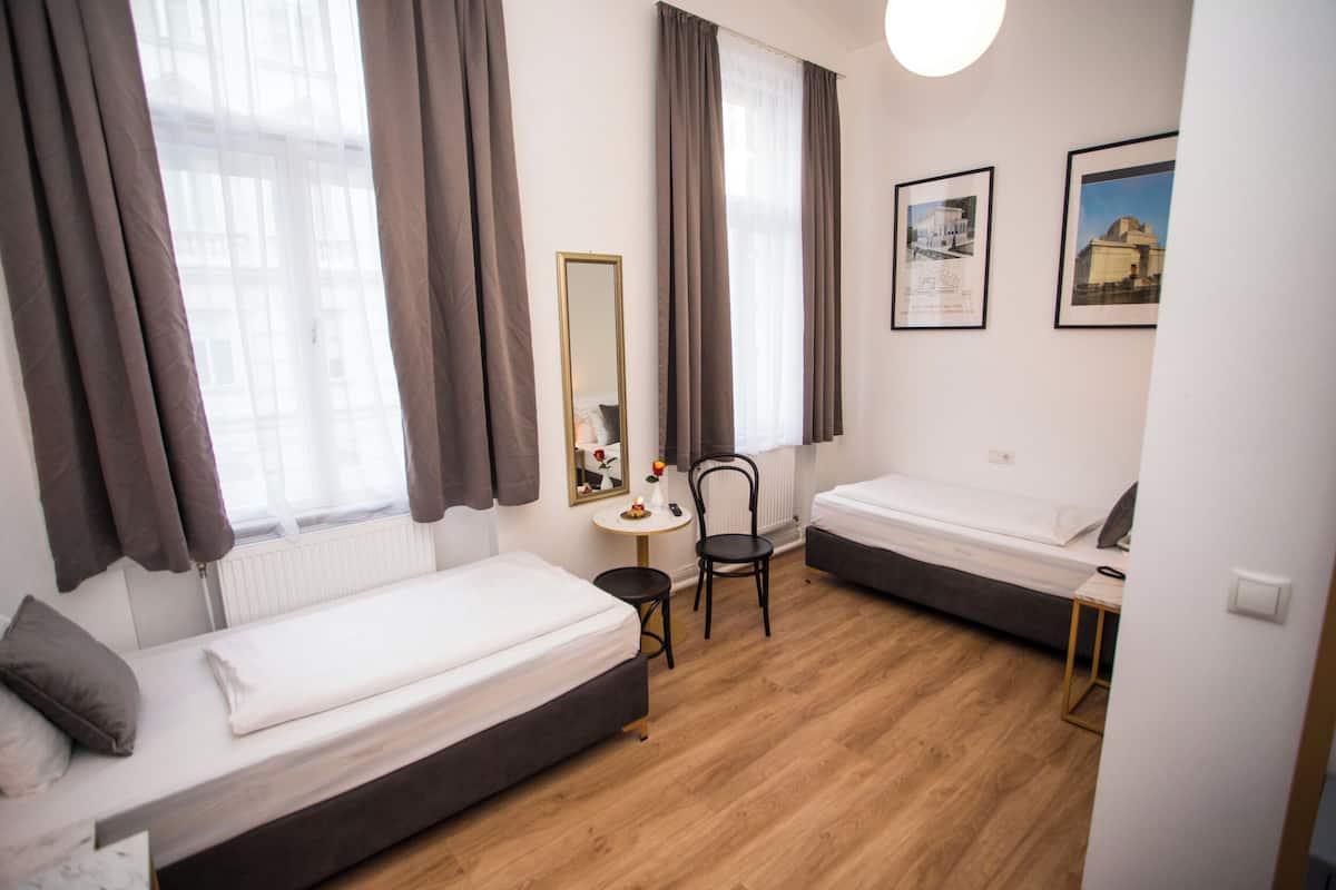 Une petite chambre moderne avec deux lits simples, une table ronde, une chaise et un grand miroir.