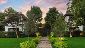 A pathway leading to a gated entrance surrounded by lush greenery and trees, with buildings on either side. - Welcome to your Dallas escape — a luxurious 1-bedroom, 1-bath condo nestled in the prestigious Swiss Ave district. Perfect for 2 guests, this retreat blends timeless elegance with modern amenities for an unforgettable stay. (Dallas)