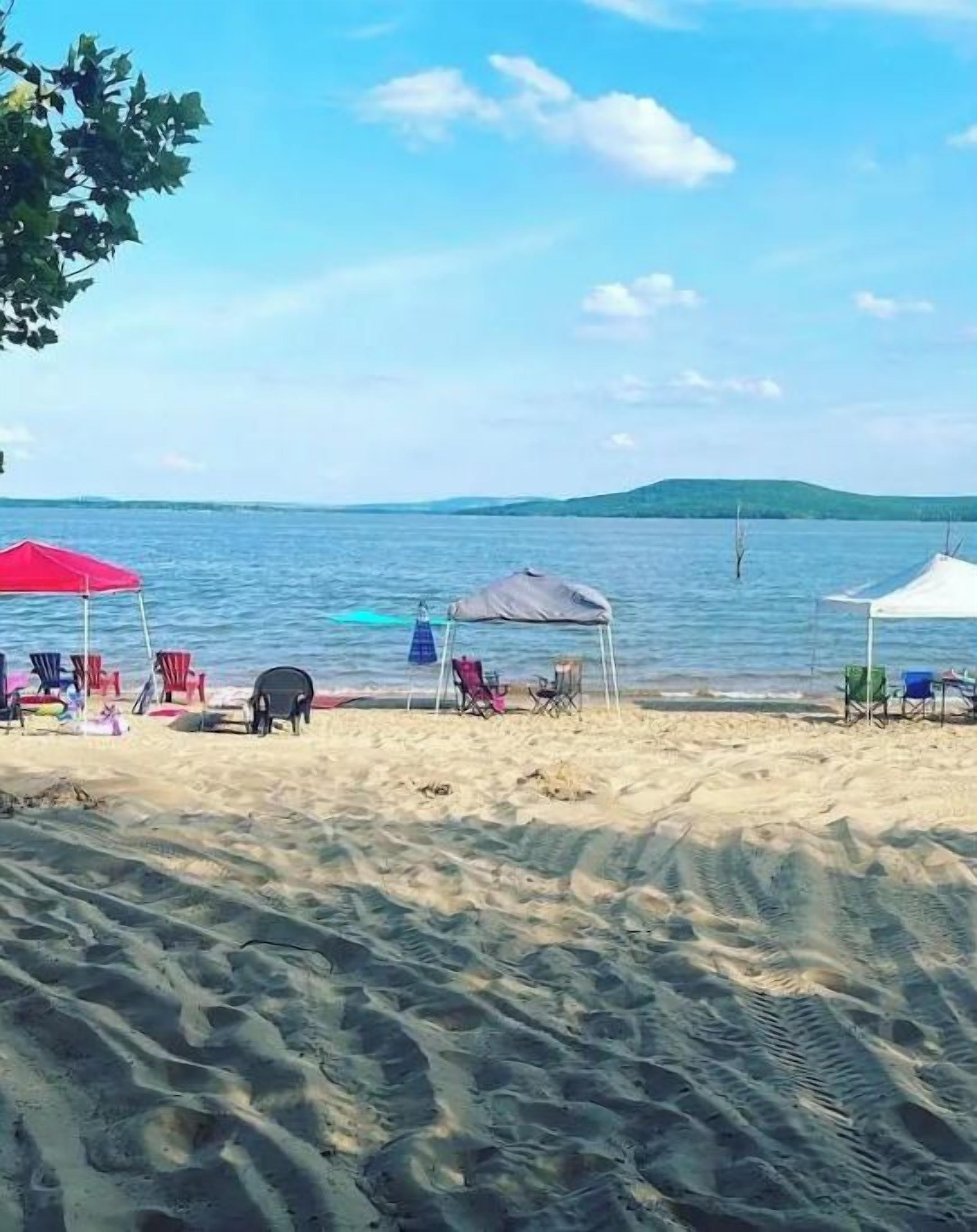 A beach with several umbrellas and chairs, a tent, and a calm sea.