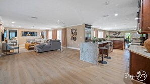 A spacious living area with a grey sofa, a coffee table, and a kitchen area with a marble island and bar stools. - 8BR Villa with Heated Pool Near Beach (Largo)